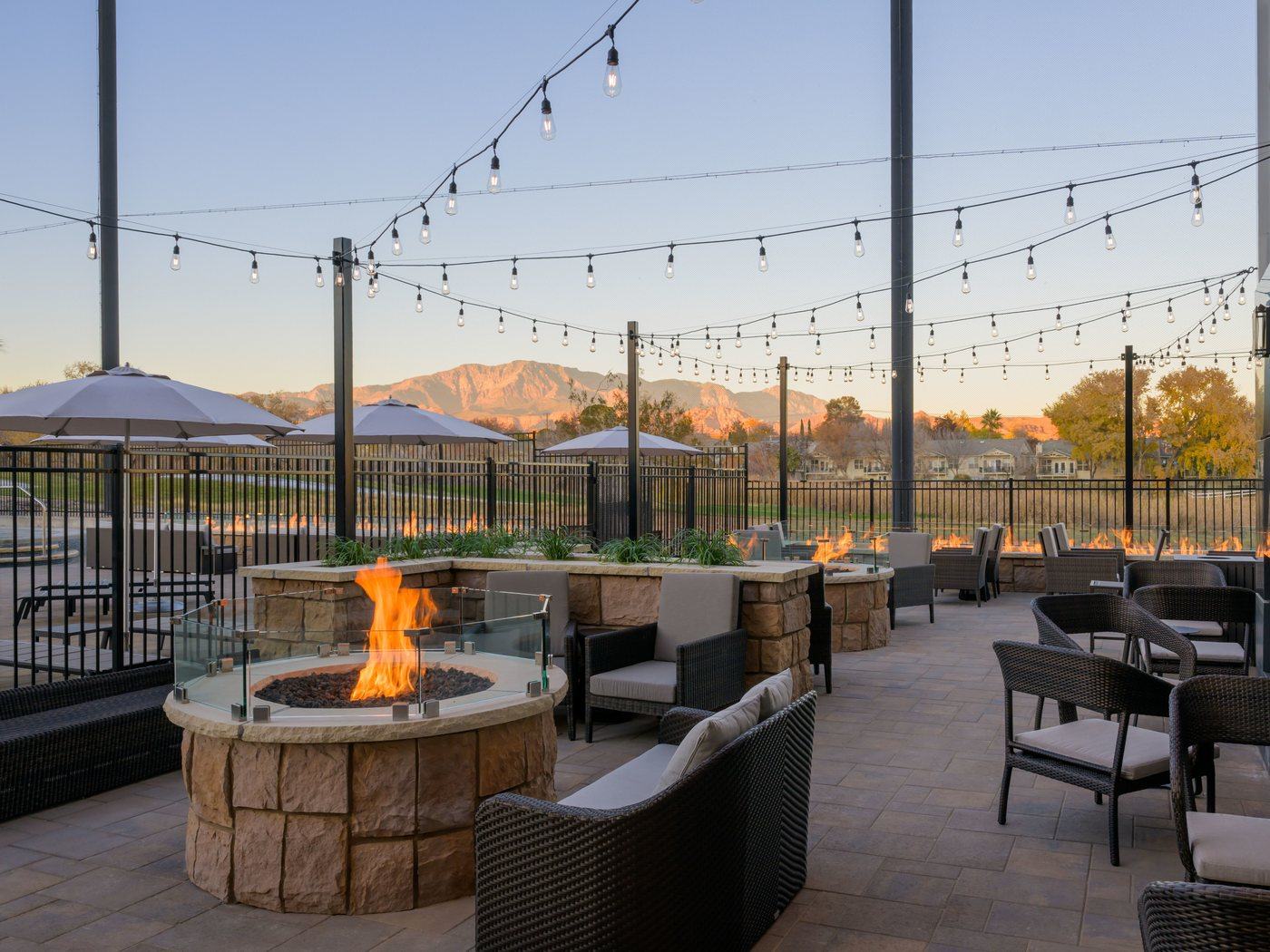 The outdoor patio at Back Nine Bistro & Bar, with gas fire pits, lounge seating and string lights against the red rock at sunset
